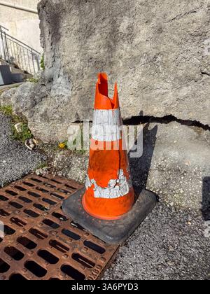 Beschädigter Traffic Kegel an der Rosty Ablaufabdeckung Stockfoto
