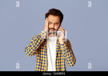 Junger Inder mit Kopfschmerzen oder Depressionen auf dem Smartphone sprechen Über fliedem Hintergrund Stockfoto