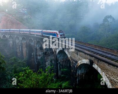 Ein landschaftlich reizvoller Zug überquert die berühmte Nine Arch Bridge in Ella, Sri Lanka, umgeben von nebeligen tropischen Wäldern, die eine Mischung aus Geschichte, Natur, und zeigen Stockfoto