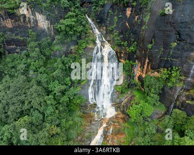 Das Bild zeigt den geheimen Wasserfall in Illukpelessa, Sri Lanka, umgeben von dichtem tropischem Grün. Das Wasser kaskadiert über zerklüftete Felsen in eine Tra Stockfoto