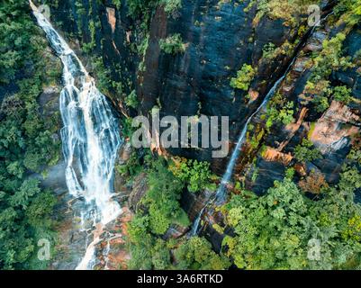 Das Bild zeigt den geheimen Wasserfall in Illukpelessa, Sri Lanka, umgeben von dichtem tropischem Grün. Das Wasser kaskadiert über zerklüftete Felsen in eine Tra Stockfoto