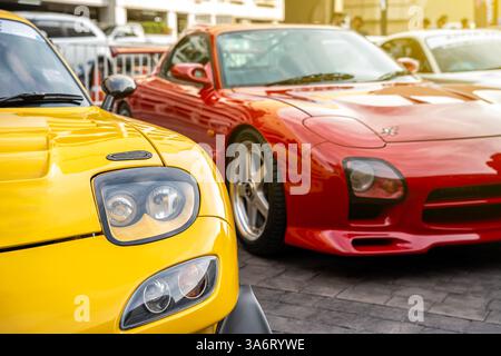 Moderne gelbe und rote Autos Nahaufnahme von Scheinwerfern und Sonnenstrahlen, die in einer Reihe im Freien geparkt sind, brandneue Autos zum Verkauf. Stockfoto