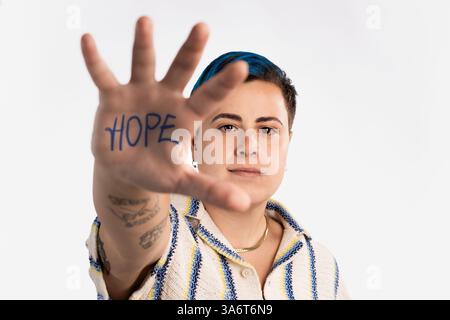 Junge Frau mit mutiger Frisur und Tätowierungen, die im weißen Studio Worthoffnungen zeigen und Aktivismus und Ermächtigung repräsentieren Stockfoto