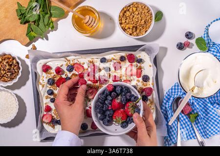 Kochen Herstellen gefrorener Joghurtrinde Hintergrund mit griechischem Joghurt, frischer Beere, Müsli, Honig, Schokoladensauce, mit Backblech Deko. Blick von oben auf die Frau Stockfoto