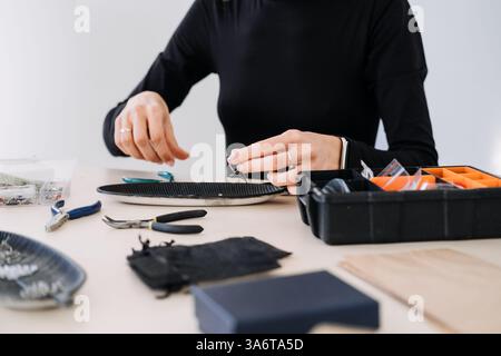 Schmuckhandwerker, der sorgfältig ein Paar handgefertigter Ohrringe zusammenstellt. Schmuckhandwerk, Handwerkskunst, handgemachte Mode, Schmuckherstellung Stockfoto