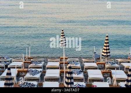 Leerer Strand in Nizza, am frühen Morgen: Reihen von Liegestühlen und Sonnenschirmen, ruhiges Meer. Stockfoto