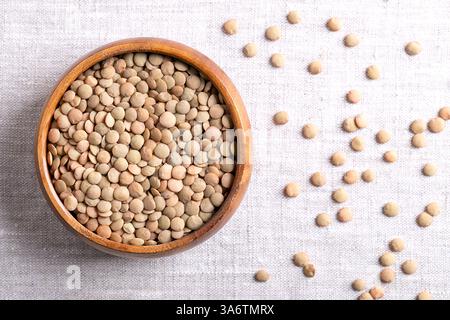 Große grüne Linsen in einer Holzschale auf Leinenstoff. Ungeschälte, getrocknete Plattenlinsen, eine in der Regel größere, flache Linsenvariante. Stockfoto