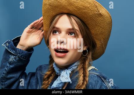 Eine junge Frau trägt eine Denim-Jacke und einen Hut und strahlt Frühlingsenergie in einem lebendigen Studio aus. Stockfoto