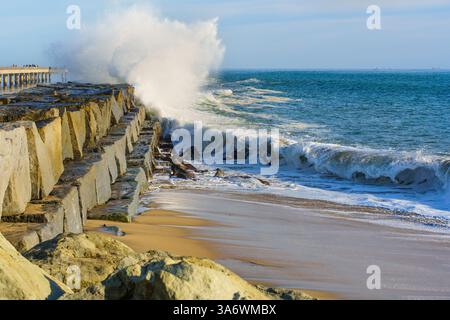 Am Cabrillo Beach Pier in San Pedro prallen dynamische Wellen gegen die felsige Küste und zeigen die natürliche Schönheit der Küste unter einem hellblauen Himmel und tra Stockfoto