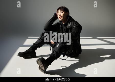 Der gutaussehende Mann sitzt lässig auf dem Boden und präsentiert ein trendiges Outfit mit selbstbewusstem Ausdruck. Stockfoto