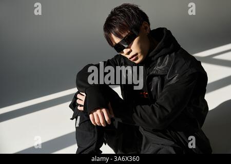 Ein hübscher junger Mann in stylischer schwarzer Kleidung trifft eine selbstbewusste Pose vor leichten Akzenten. Stockfoto