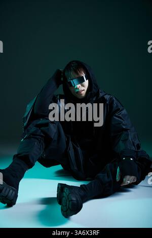 Ein hübscher junger asiatischer Mann in einem scharfen schwarzen Outfit trifft bei schlechten Lichtverhältnissen eine modische Pose. Stockfoto