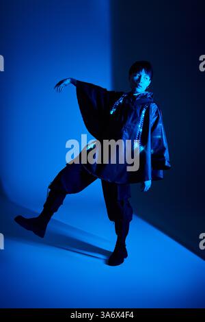 Ein stilvoller junger asiatischer Mann posiert in modernem Outfit unter markanten blauen Lichtern. Stockfoto