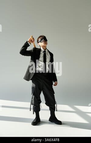 Ein junger asiatischer Mann im Anzug posiert selbstbewusst, während er ein stilvolles Accessoire hält. Stockfoto