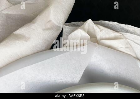 Nahaufnahme einer zerknitterten weißen Papierserviette mit Textur, Falten und weichen Papierdetails für abstrakte Designs. Stockfoto
