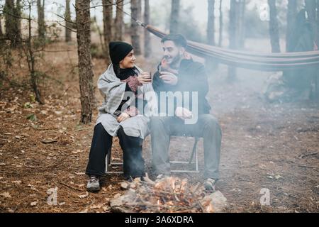 Ein junges Paar genießt ein warmes Getränk am Lagerfeuer im Wald Stockfoto