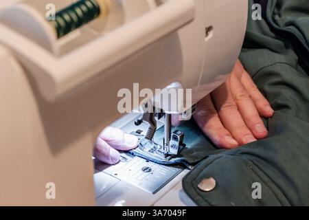 Mann, der eine Nähmaschine mit einem Kleidungsstück benutzt, für Reparaturen, Anpassungen, Kreationen, Upcycling Stockfoto