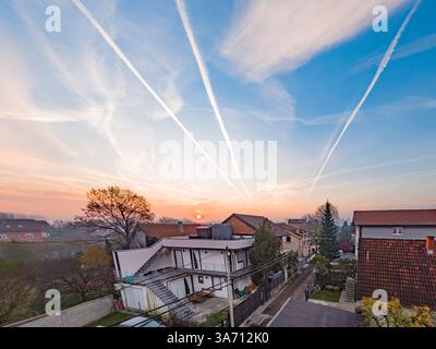 Feuriger Sonnenuntergang über Vorstadthäusern mit dramatischen Kondensstreifen über dem farbenfrohen Himmel. Stockfoto