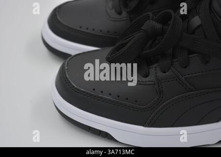 Schöne, junge Sportschuhe, schwarze Stiefel mit weißen harten Sohlen sind auf einem weißen plasti.. Warme Halbstiefel aus Leder mit Isolierung. Stockfoto