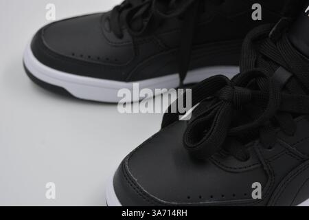 Schöne, junge Sportschuhe, schwarze Stiefel mit weißen harten Sohlen sind auf einem weißen plasti.. Warme Halbstiefel aus Leder mit Isolierung. Stockfoto