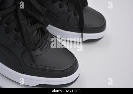 Schöne, junge Sportschuhe, schwarze Stiefel mit weißen harten Sohlen sind auf einem weißen plasti.. Warme Halbstiefel aus Leder mit Isolierung. Stockfoto