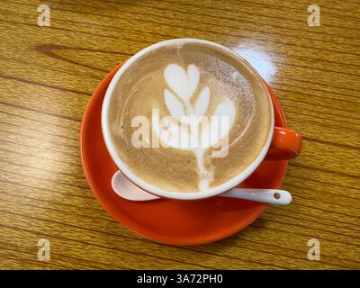 Köstlicher Kaffee mit Latte Art serviert in einer lebendigen Orangenschale in einem gemütlichen Café. Stockfoto