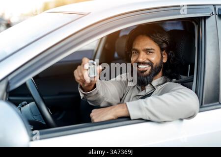 Glücklicher junger indianer, der im Auto sitzt und den Schlüssel aus dem Fahrzeugfenster zeigt Stockfoto