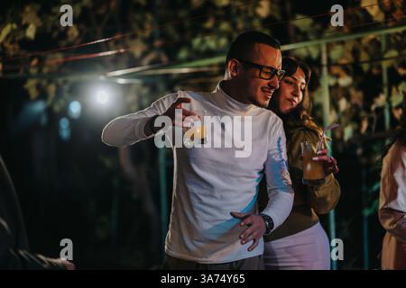 Junge Freunde genießen Drinks und tanzen im Freien in einer lebhaften Atmosphäre Stockfoto