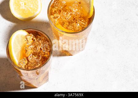 Eistee mit Zitrone. Gläser süßen Eistees mit Zitronenscheiben und zerstoßenem Eis auf weißem Hintergrund mit trendigem Sonnenlicht, Kopierraum. Hausgemachter Sommer c Stockfoto