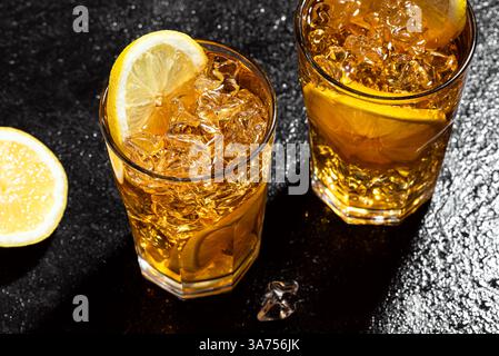 Eistee mit Zitrone. Gläser süßen Cocktail-Eis-Tee mit Zitronenscheiben und zerstoßenem Eis auf nassem schwarzem Schieferhintergrund, Draufsicht, Kopierraum. Hausgemacht Stockfoto