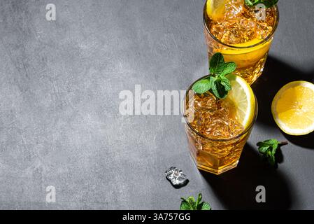 Long Island Ice Tea Cocktail Drink. Zwei Gläser Eistee mit Zitrone, Minze und Eis auf schwarzem Schieferhintergrund, Draufsicht, Kopierraum. Hausgemachter Sommer Stockfoto