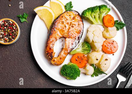 Gegrilltes Lachsfischsteak mit gedämpftem Gemüse auf dunklem Hintergrund, Blick von oben. Gesunde Fitness-Lebensmittel, Keto Diät Mahlzeit Konzept. Stockfoto
