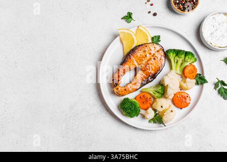 Gegrilltes Lachsfischsteak mit gedämpftem Gemüse und Tzatziki-Sauce auf weißem Hintergrund, Blick von oben. Gesunde Ernährung, Keto Diät Mahlzeit Konzept. Stockfoto
