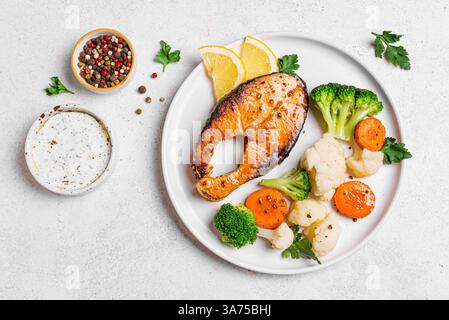 Gegrilltes Lachsfischsteak mit gedämpftem Gemüse und Tzatziki-Sauce auf weißem Hintergrund, Blick von oben. Gesunde Ernährung, Keto Diät Mahlzeit Konzept. Stockfoto