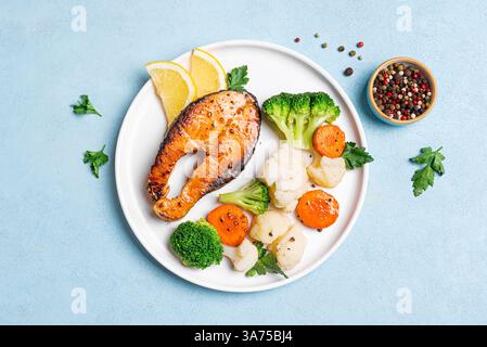 Gegrilltes Lachsfischsteak mit gedämpftem Gemüse auf blauem Hintergrund, Blick von oben. Gesunde Fitness-Lebensmittel, Keto Diät Mahlzeit Konzept. Stockfoto