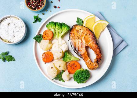 Gebratenes Lachsfischsteak mit gedämpftem Gemüse auf blauem Hintergrund, Blick von oben. Gesunde Fitness-Lebensmittel, Keto Diät Mahlzeit Konzept. Stockfoto