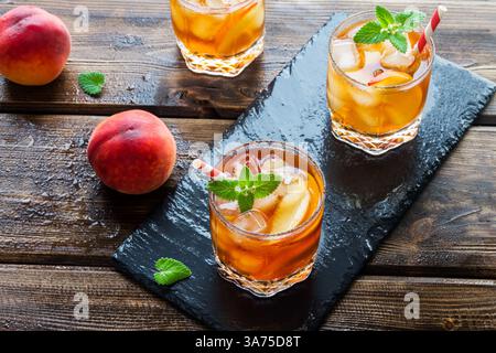 Eistee mit Pfirsich. Gläser süßen Eistees mit Pfirsichscheiben, Minze und Crash Eis auf Schieferhintergrund, Blick von oben. Hausgemachtes kaltes Sommergetränk. Stockfoto