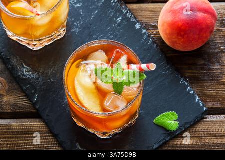 Eistee mit Pfirsich. Gläser süßen Eistees mit Pfirsichscheiben, Minze und Crash Ice aus nächster Nähe, Blick von oben. Hausgemachtes kaltes Sommergetränk. Stockfoto