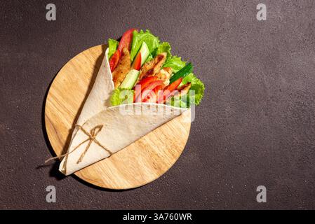 Gegrilltes Hühnchen und Gemüse Salat Tortilla Wrap auf dunklem hölzernem Hintergrund, Draufsicht, Kopierraum. Frisches Shawarma-Sandwich. Griechische Gyros Roll. Stockfoto