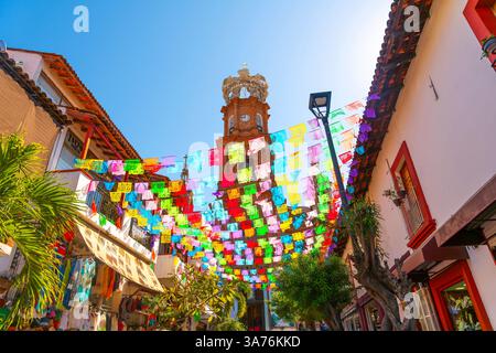 Blick von unten auf die Kirche unserer Lieben Frau von Guadalupe mit farbenfrohen Fahnen, die an einem sonnigen Morgen in Puerto Vallarta Mexiko auf der anderen Straßenseite aufgereiht sind. Stockfoto