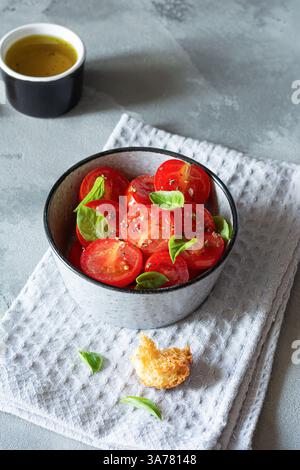Salat aus frischen Kirschtomaten mit Croutons, Basilikumblättern, Gewürzen und aromatischem Olivenöl auf grauem Hintergrund. Panzanella ist ein toskanischer Gemüsesalat Stockfoto