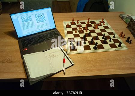 Solitär-Schachtraining mit einem Computer und echten Holzstücken auf einem Schachbrett. Stockfoto