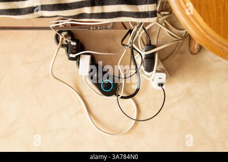 Ein Verlängerungskabel mit eingeschalteten Geräten und ein Adapter auf dem Boden vermischt mit vielen Drähten, verwickelte Drähte in der Verlängerungskabelbuchse zu Hause an Stockfoto
