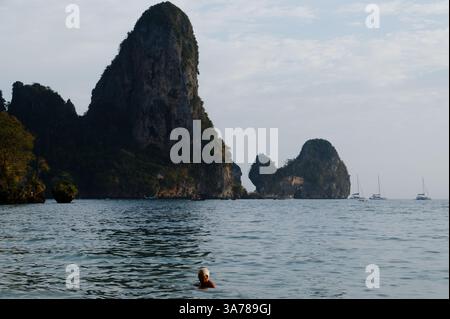 Reife Schwimmer schweben im ruhigen Wasser vor Tonsai Beach, umgeben von hohen Kalksteinklippen und weit entfernten, verankerten Segelbooten Stockfoto