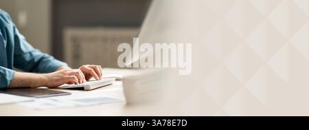 Junger Mann, der am Schreibtisch sitzt und auf der Computertastatur schreibt Stockfoto