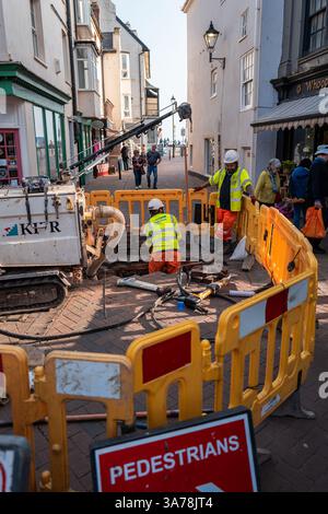 Zwei Mitarbeiter der Straßeninstandhaltung im Südwesten, umgeben von gelben Verkehrsbarrieren, graben ein Loch in der Main Street von Sidmouth, Devon, Großbritannien. Stockfoto