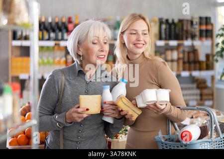 Zwei Käuferinnen mit verschiedenen Milchprodukten in den Händen treffen weiterhin die Wahl in der Lebensmittelabteilung des Supermarktes Stockfoto