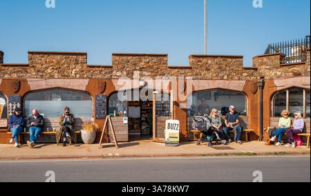 Leute, die an einem sonnigen Tag im Frühjahr vor einem Strandcafé in Sidmouth sitzen. East Devon, England, Großbritannien. Stockfoto