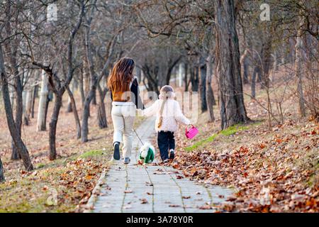 Glückliche Familie mit zwei Kindern, die gemeinsam im Herbstpark einem Hund nachjagen Stockfoto