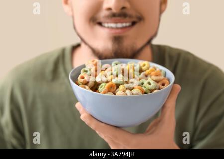 Mann hält Schüssel mit Müsliringen im Wohnzimmer, Nahaufnahme Stockfoto